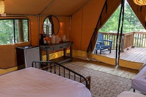 Ein Zelt mit Bett, Kommode und Stuhl auf einer Terrasse mit Blick auf Bäume.