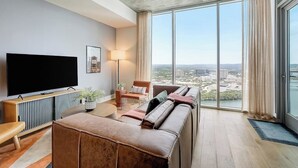 Un soggiorno moderno con una grande TV a schermo piatto, un divano, un tavolino da caffè e vista sulla città attraverso ampie finestre.