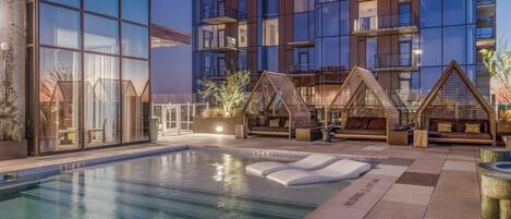 Un bâtiment moderne doté d’une piscine, d’un espace extérieur aménagé et d’une façade en verre.
