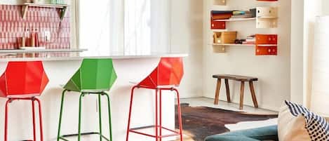 A modern living space with a kitchen area, wooden flooring, and colorful stools.