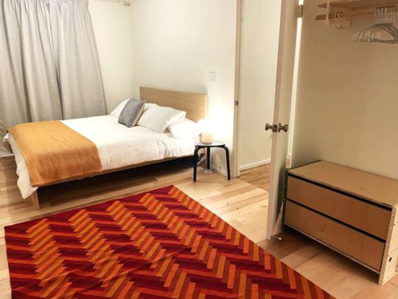 A bedroom with a bed, a small bedside table, a dresser, and a patterned rug.