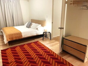 A bedroom with a bed, a small bedside table, a dresser, and a patterned rug.