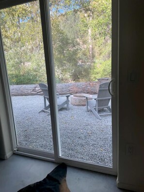 A room with a sliding glass door leading to an outdoor patio with two Adirondack chairs and a stone fire pit.