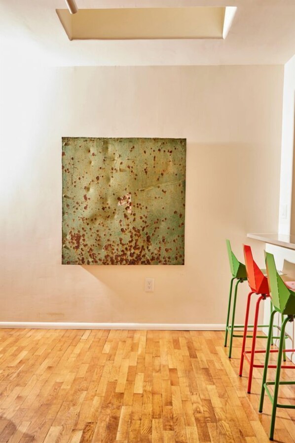 Una habitación con piso de parquet de madera, una silla verde y roja, y una obra de arte colgada en la pared.