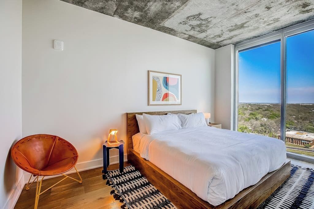 Ein Schlafzimmer mit einem großen Bett, einem Sessel, einem Nachttisch, einem Gemälde und Blick auf die Landschaft.