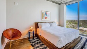 A bedroom with a large bed, a chair, a nightstand, a painting, and a view of the landscape. - Austin hideaway in the heart of the city with rooftop pool, terrace, and gym (Austin)