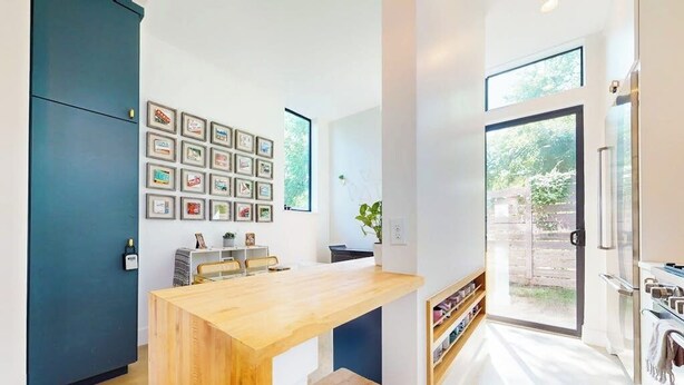 A modern kitchen with a wooden table, a blue cabinet, and a wall of framed pictures. - Modern two story home with kitchen, gated yard, balcony, close to South Congress (Austin)