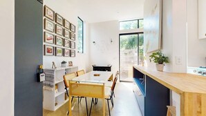A modern kitchen with a dining area, a white wall with framed pictures, and a large window. - Modern two story home with kitchen, gated yard, balcony, close to South Congress (Austin)