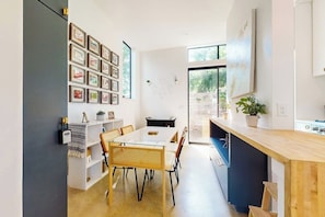 Eine moderne Küche mit Essbereich, einer weißen Wand mit gerahmten Bildern und einem großen Fenster.