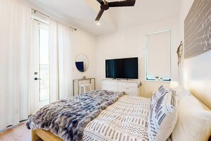 Ein Schlafzimmer mit Bett, Fernseher, Deckenventilator, Spiegel und Fenster.