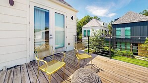 A wooden deck with outdoor seating, a white building with a glass door, and a modern house in the background. - Modern two story home with kitchen, gated yard, balcony, close to South Congress (Austin)