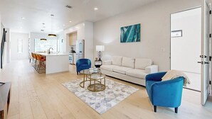 A modern living room with a sofa, blue armchairs, a coffee table, and a kitchen in the background. - Fantastic townhouse with enclosed backyard and high-speed internet (Austin)