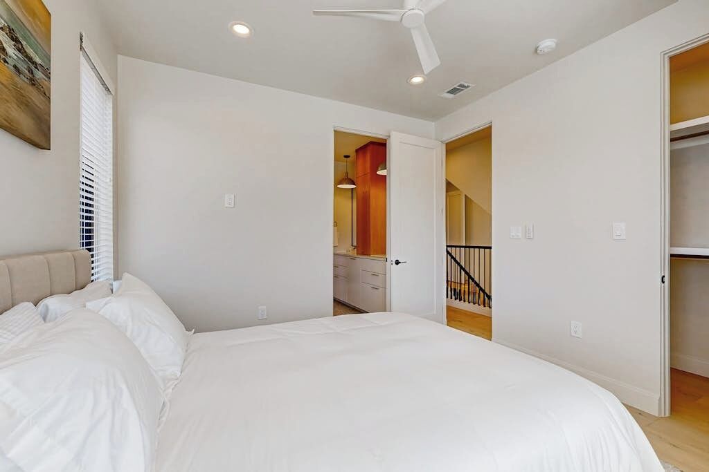 Une chambre avec un lit, un ventilateur de plafond et une vue sur une cuisine et un escalier.