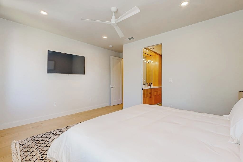 A bedroom with a bed, a ceiling fan, recessed lighting, a door, and a small mirror.