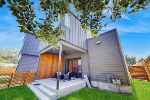 Ein modernes, zweistöckiges Haus mit überdachter Terrasse, Holzdeck und umzäunter Garten.