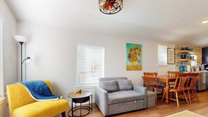 A living room with a sofa, armchair, dining table, chairs, and a kitchen area. - Modern cozy house with full kitchen, dining & living area, TV, close to downtown (Austin)
