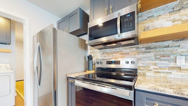 A modern kitchen with stainless steel appliances, a stone backsplash, and dark wood cabinetry. - Modern cozy house with full kitchen, dining & living area, TV, close to downtown (Austin)