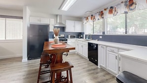 Una cocina moderna con armarios blancos, una mesa de comedor de madera y un lavavajillas negro.