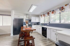 A modern kitchen with white cabinets, a wooden dining table, and a black dishwasher. - Cozy home with enclosed backyard and fire pit - Dog-friendly (Austin)
