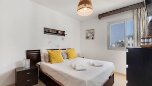 A bedroom with a bed, bedside table, wall-mounted shelf, and a window with curtains. - Charming 2-bedroom Apartment With Ocean Views in Adeje (Adeje)