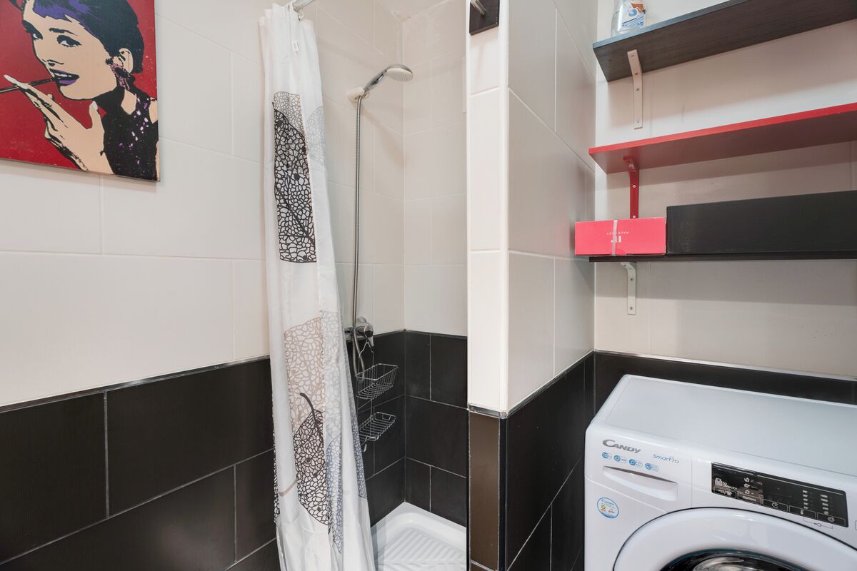 Een badkamer met een douche, toilet, wasmachine en een plank met toiletartikelen.