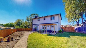 Une maison à deux étages dotée d’un patio couvert, d’une cour arrière clôturée et d’une pelouse bien entretenue.