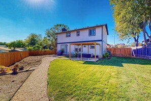 Ein zweistöckiges Haus mit überdachter Terrasse, umzäunter Garten und gepflegtem Rasen.