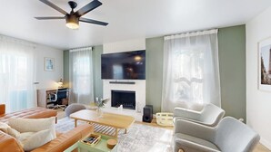 Un salon moderne comprenant un canapé, un fauteuil, une table basse, une cheminée, un téléviseur et un ventilateur de plafond.
