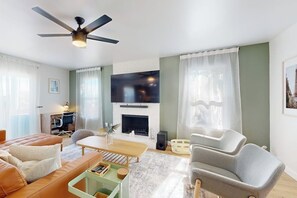 Ein modernes Wohnzimmer mit Sofa, Sessel, Couchtisch, Kamin, Fernseher und Deckenventilator.
