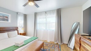 Une chambre d’hôtel équipée d’un lit, d’un bureau, d’un ventilateur de plafond, d’une fenêtre avec des rideaux et d’un téléviseur.