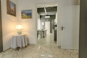 A hallway with a table and lamp, a dining area with chairs, and a kitchen area with cabinets and a door. - GuestHost - La Rotonda Cozy Apartment in Marsala (Marsala)