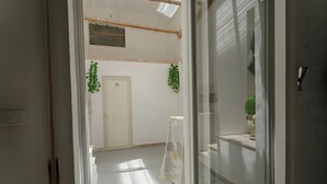 Een gang met een deur, een kleine plant en een ladder tegen de muur.