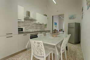 A modern kitchen with white cabinets, a stainless steel refrigerator, and a dining table with chairs. - GuestHost - La Rotonda Cozy Apartment in Marsala (Marsala)