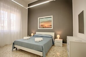 Ein Schlafzimmer mit einem Bett, Nachttischlampen, einem Nachttisch, einer Kommode und einem gerahmten Bild an der Wand.