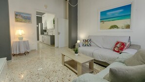 Een moderne woonkamer met een bank, een salontafel, een lamp en een schilderij van een strand.