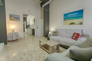 A modern living room with a sofa, a coffee table, a lamp, and a painting of a beach. - GuestHost - La Rotonda Cozy Apartment in Marsala (Marsala)
