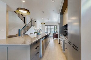 A modern kitchen with a central island, stainless steel appliances, and a staircase with a black railing. - Two modern townhouses with enclosed backyards (Austin)