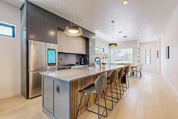 A modern kitchen with a central island, stainless steel appliances, and a dining area with bar stools. - Two modern townhouses with enclosed backyards (Austin)