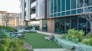 Un edificio moderno con amplios ventanales, un patio ajardinado con asientos exteriores y diversas plantas.