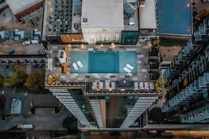 Ein Hochhaus mit einem Pool auf dem Dach, Sitzgelegenheiten im Freien und Blick auf die umliegende Stadt.