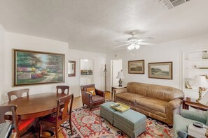 Ein Wohnzimmer mit Esstisch, Sofa, Couchtisch und Deckenventilator.