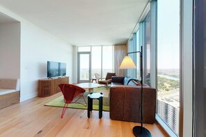 Ein modernes Wohnzimmer mit einer Couch, Sesseln, einem Fernseher und einem großen Fenster mit Blick auf die Stadt.