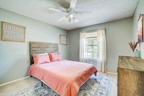 Un dormitorio con cama, ventilador de techo, ventana con cortinas y cabecera de madera.