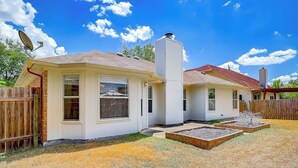 Una casa de dos pisos con antena parabólica, chimenea y un patio cercado con jardines elevados.