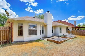 A two-story house with a satellite dish, a chimney, and a fenced yard with raised garden beds.