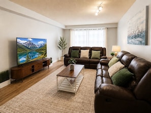 Ein Wohnzimmer mit Fernseher, Ledersofa, Couchtisch und einer Pflanze.