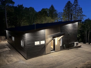 A modern, dark-colored cabin with a large open door, a small attached structure, and a sloped roof. - Spa & Nature | Asini-Nibi (Ferme-Neuve)