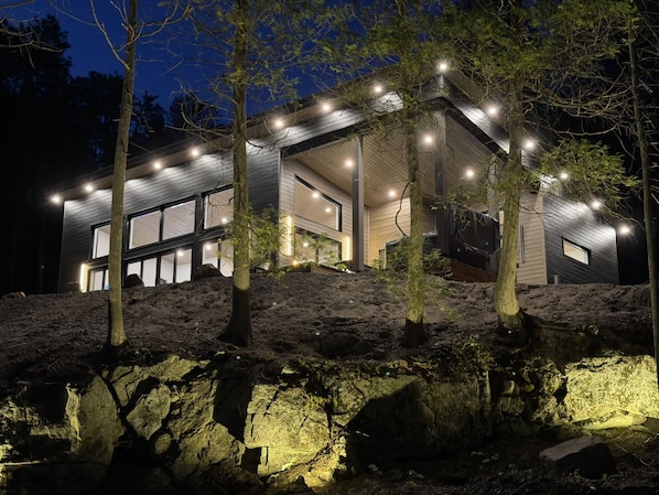 A modern house with large windows, a sloped roof, and a stone foundation. - Spa & Nature | Asini-Nibi (Ferme-Neuve)
