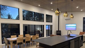 A modern kitchen with a large island, wooden chairs, and pendant lighting.