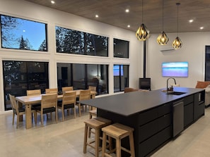 A modern kitchen with a large island, wooden chairs, and pendant lighting. - Spa & Nature | Asini-Nibi (Ferme-Neuve)